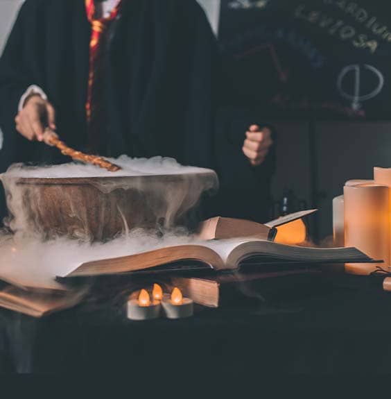 Un élève des cours de magie de La manOEuvre tend sa baguette magique devant un chaudron en lisant son livre